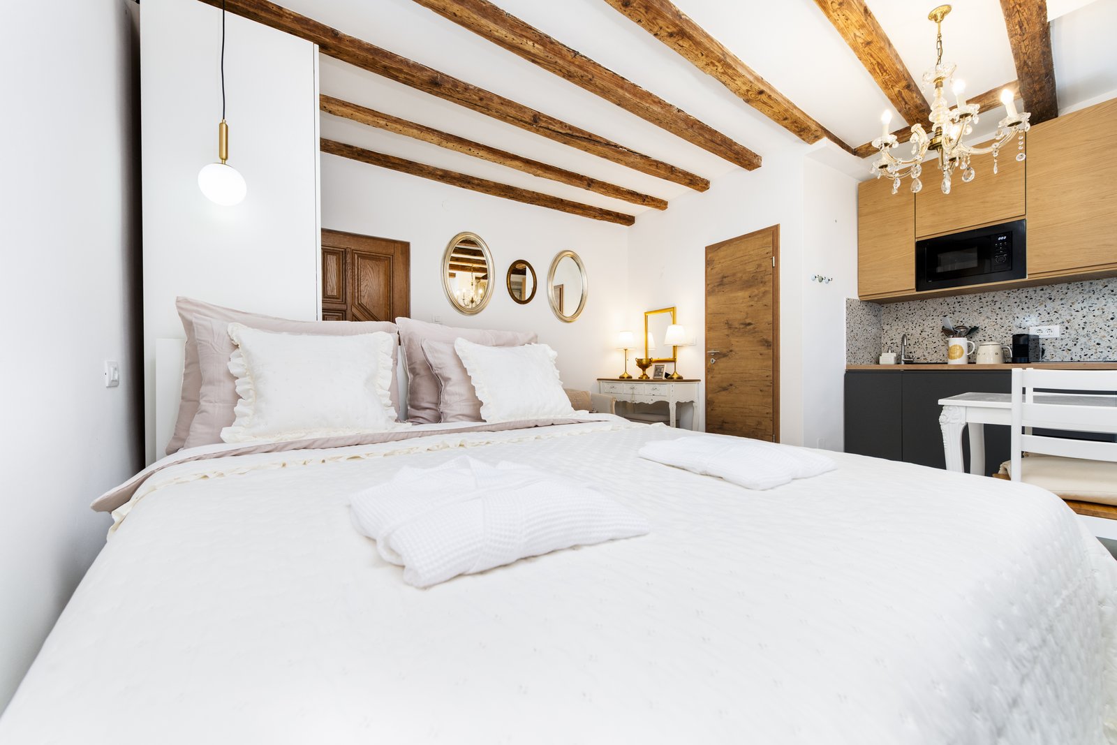 Bedroom with white linen bed beneath exposed beams and a small chandelier