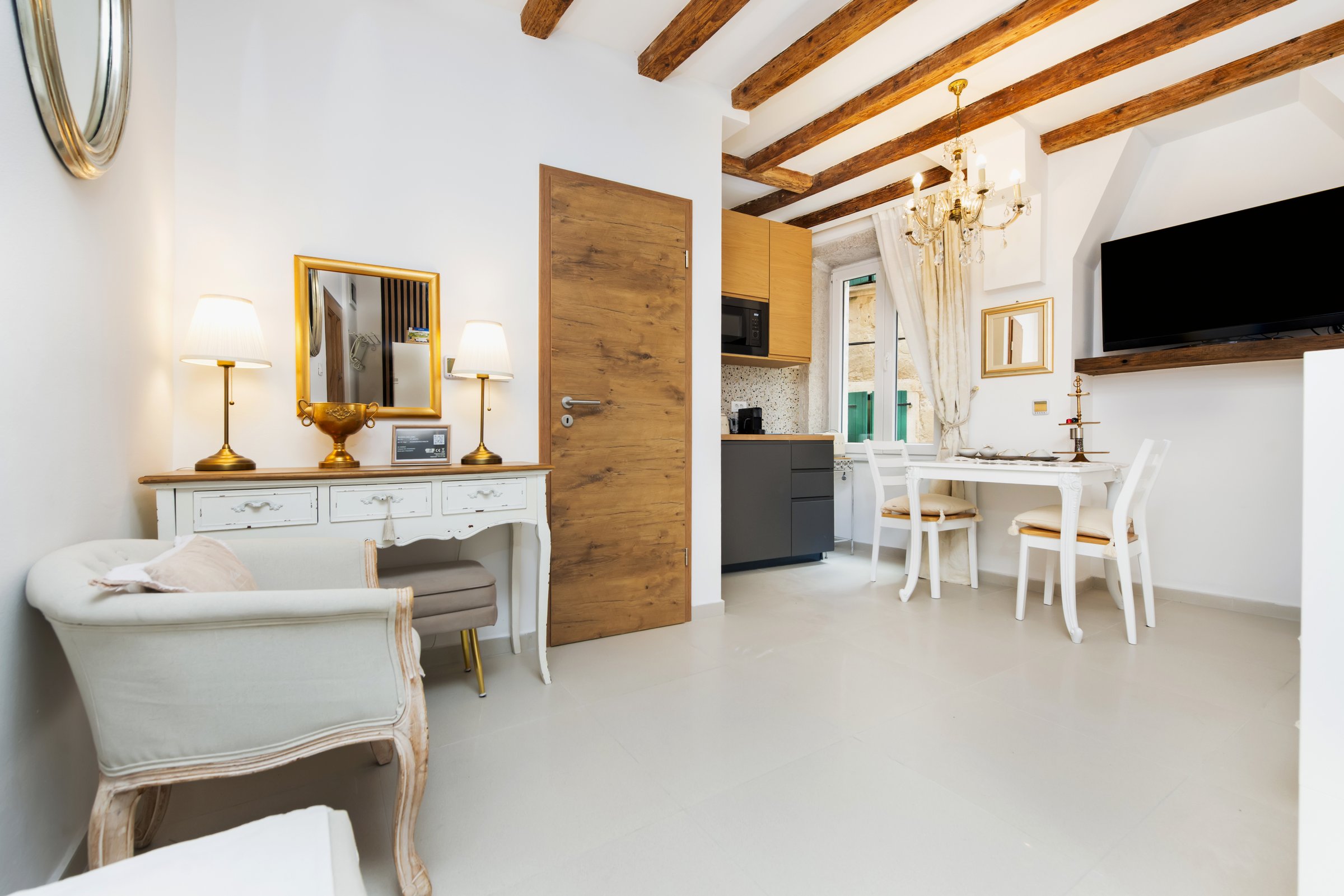 Living and kitchen area of Studio 15, with exposed wooden beams and a crystal chandelier